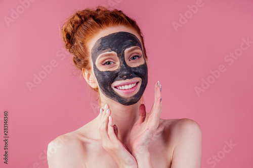 redhaired ginger young caucasian woman with natural anti acne mask on her pretty perfect face in studio pink background