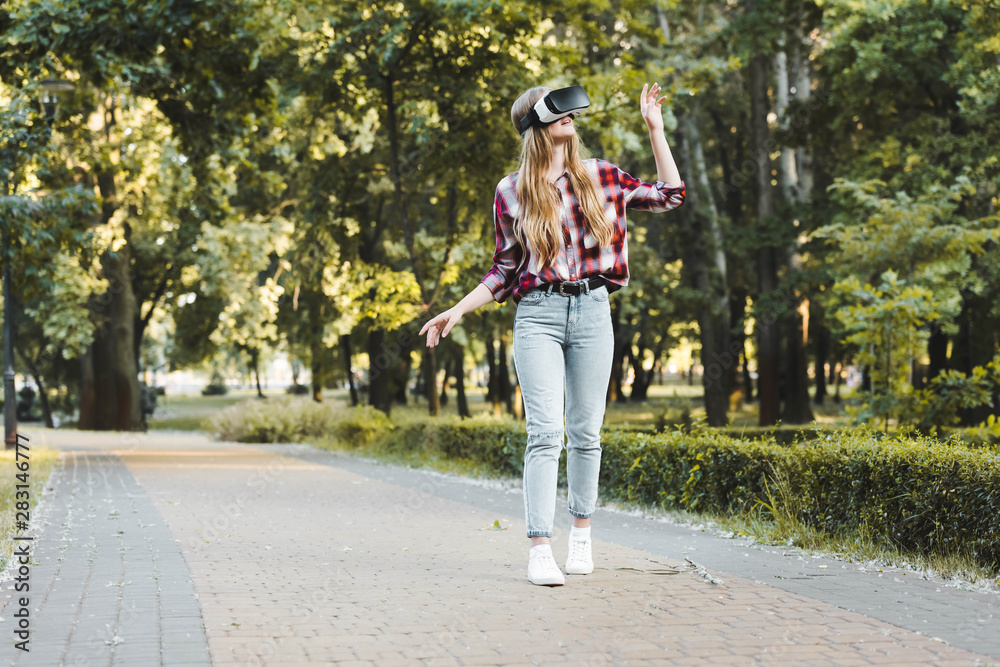 Obraz premium full length view of girl in casual clothes using vr headset while walking in park