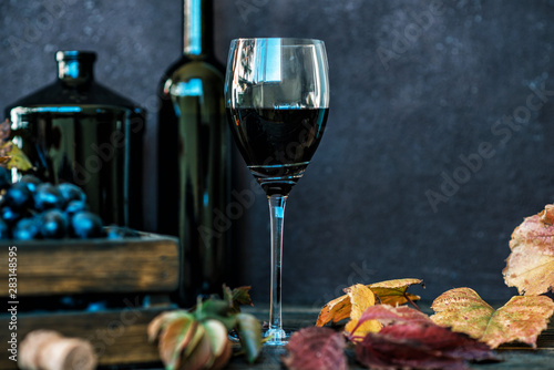 Red wine with bottle, glass and grapes on wooden background. Wine header image. Wineglass. Display in a winery or tavern of red grapes in a wooden box. Concept of the grape harvest, wine making.
