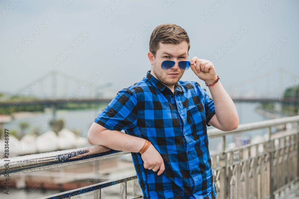 Portrait of young modern handsome man in blue plaid shirt and jeans at the city. Citizen lifestyle 