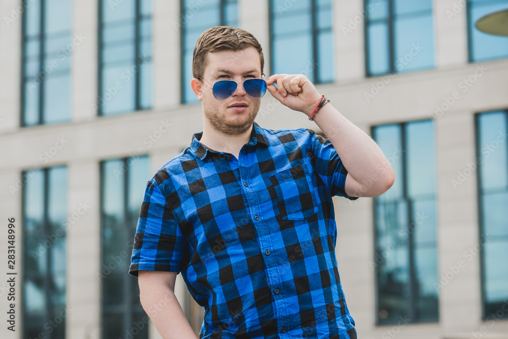 Portrait of young modern handsome man in blue plaid shirt and jeans at the city. Citizen lifestyle Portrait of young modern handsome man in blue plaid shirt and jeans at the city. Citizen lifestyle