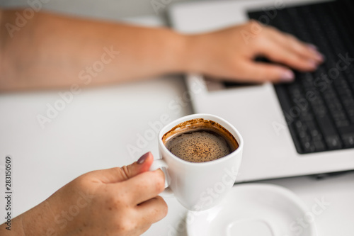 Caffeine addiction. Woman drinking coffee during work time and typing on laptop. Unhealthy eating habits, health care concept