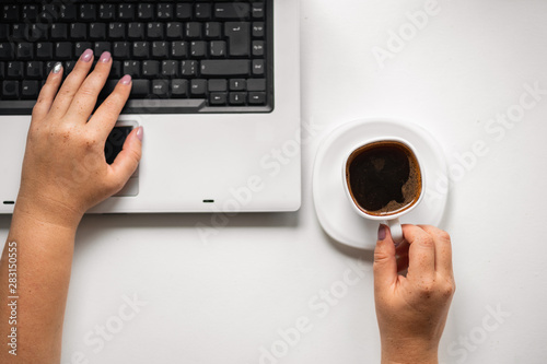 Coffee break at workplace. Woman typing on laptop and holding cup with hot drink. Eating habits, snacking, caffeine addiction, inspiration and morning routine