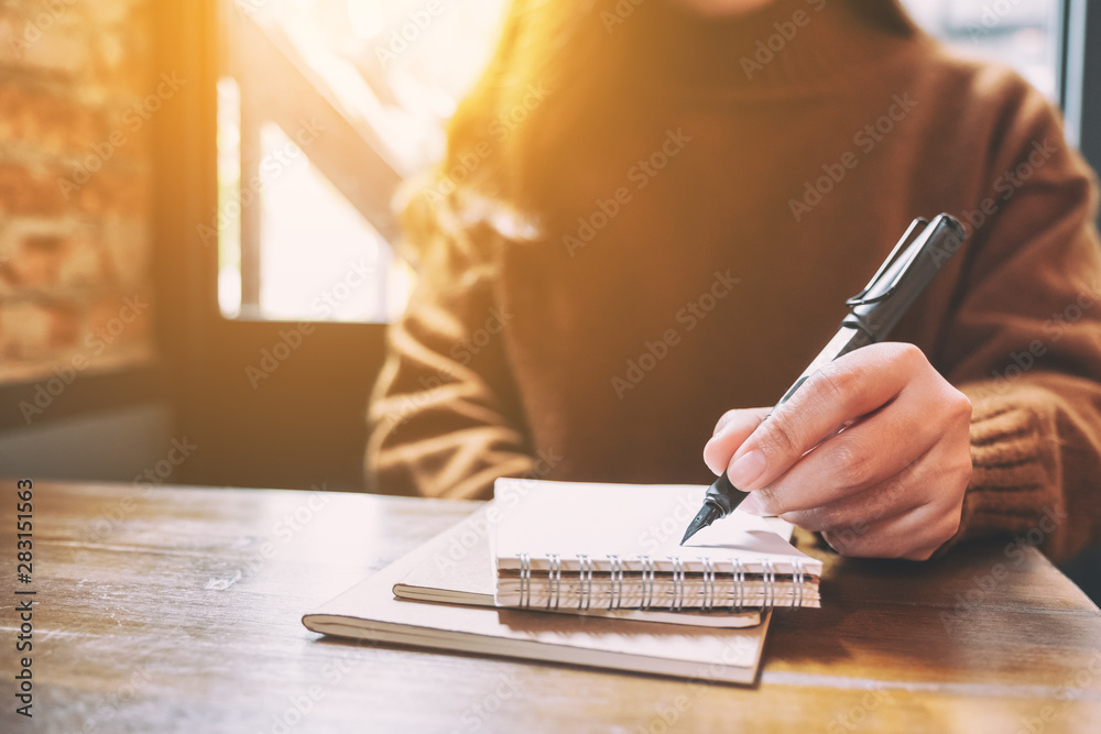 Fototapeta premium Closeup image of a woman writing on blank notebook with fountain pen on wooden table