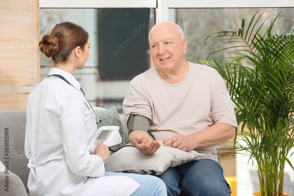 Obraz premium Nurse measuring blood pressure of elderly man in living room. Assisting senior generation