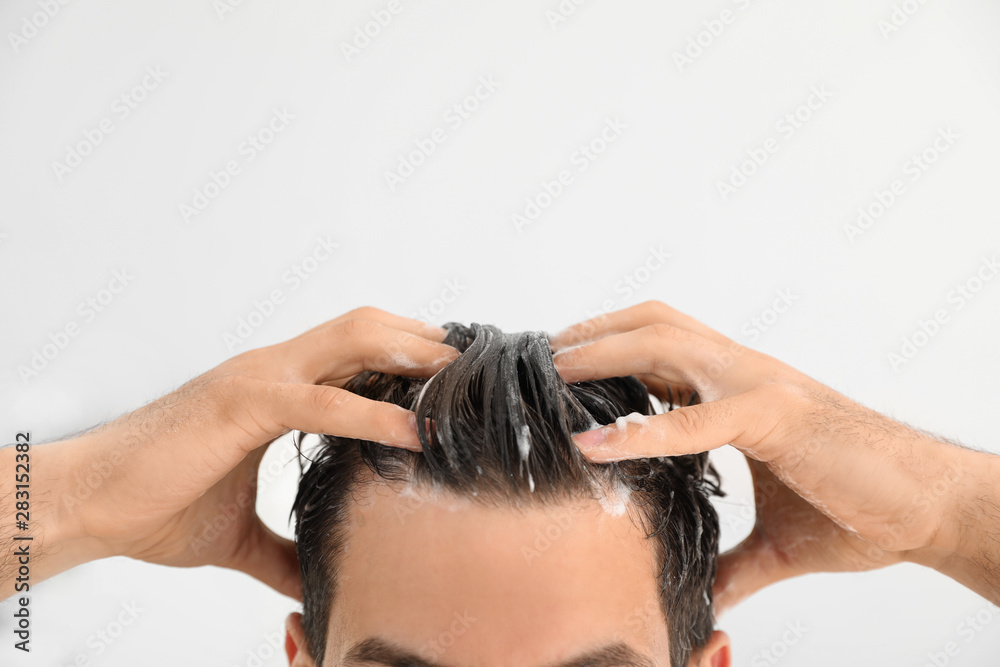 Naklejka premium Man applying shampoo onto his hair against light background, closeup. Space for text