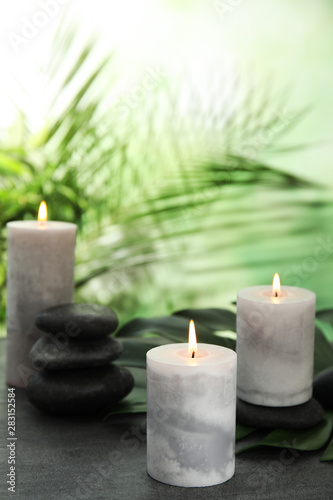 Burning candles and spa stones on grey table against blurred green background  space for text