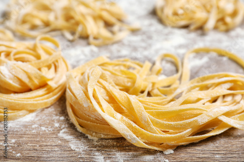 Uncooked noodles and flour on wooden table, closeup