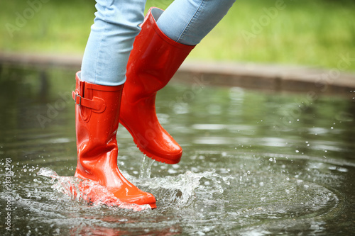 Woman with red rubber boots jumping in puddle, closeup. Rainy weather