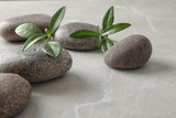 Spa stones and green leaves on grey table, space for text