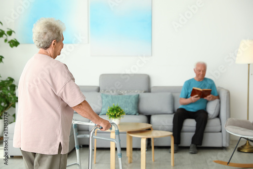 Elderly woman using walking frame and her husband at home