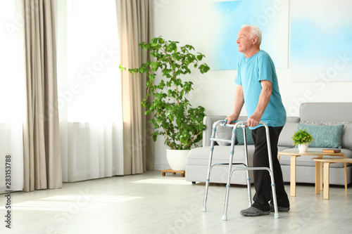 Elderly man using walking frame indoors. Space for text