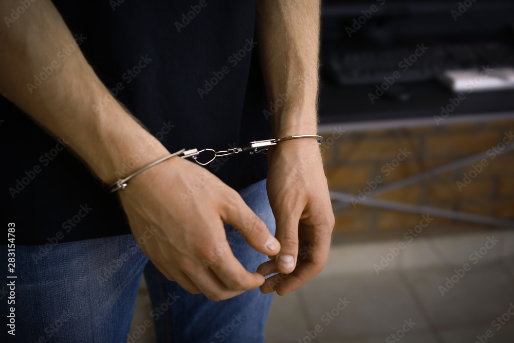 Man detained in handcuffs indoors, space for text. Criminal law