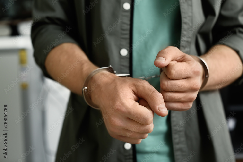 Man detained in handcuffs indoors, closeup view. Criminal law