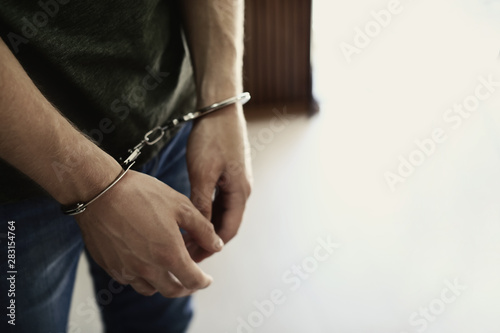 Man detained in handcuffs indoors, space for text. Criminal law photo