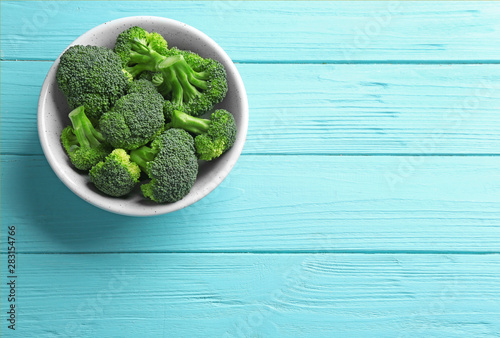 Bowl of fresh green broccoli on blue wooden table, top view. Space for text
