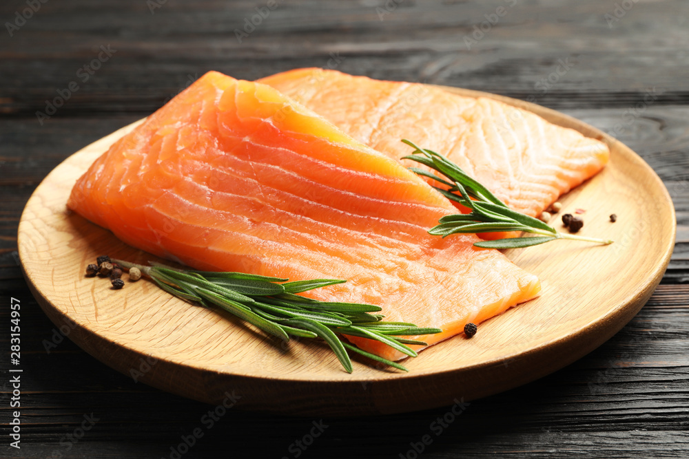 Wooden plate with tasty salmon fillet on black table, closeup