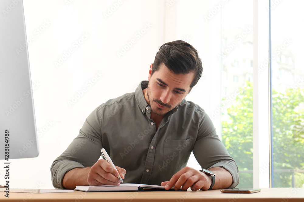 Handsome young man working with notebook at table in office Handsome young man working with notebook at table in office