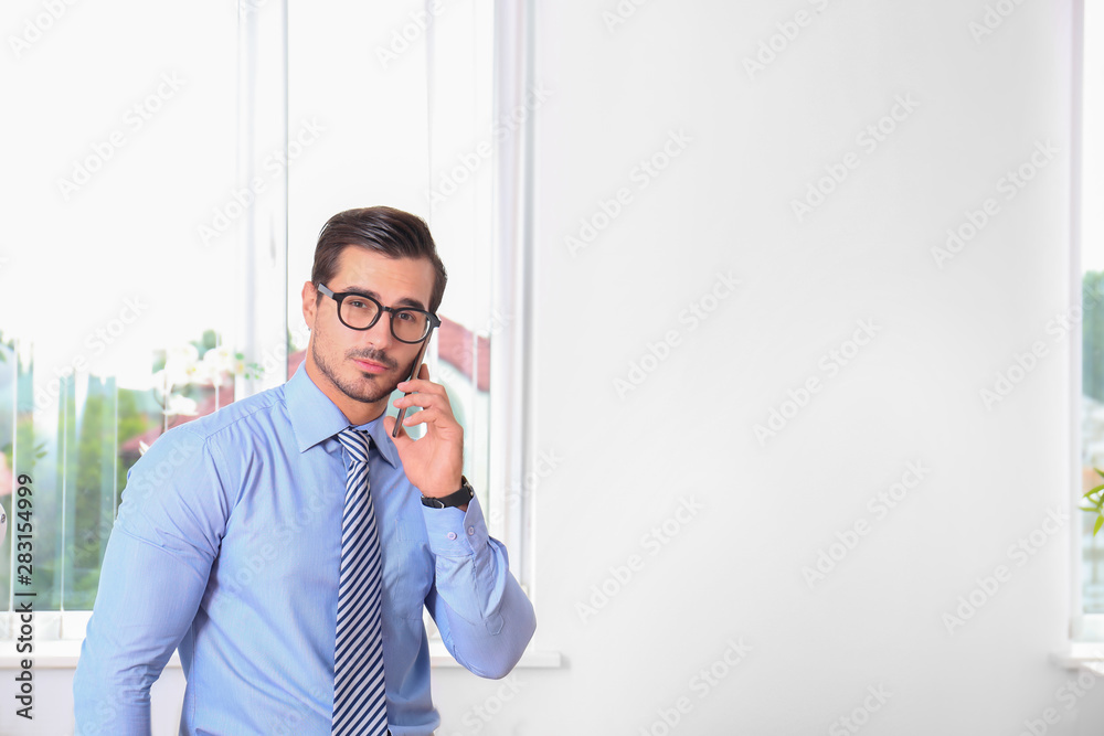 Handsome young man talking on phone at workplace, space for text Handsome young man talking on phone at workplace, space for text