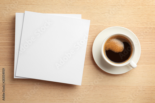 Blank paper sheets for brochure and cup of coffee on wooden background  flat lay. Mock up