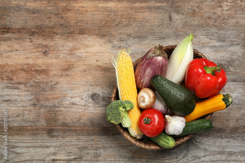 Wicker bowl with different fresh vegetables on wooden background  top view. Space for text