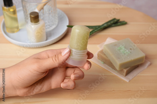 Young woman holding natural crystal alum deodorant at wooden table  closeup