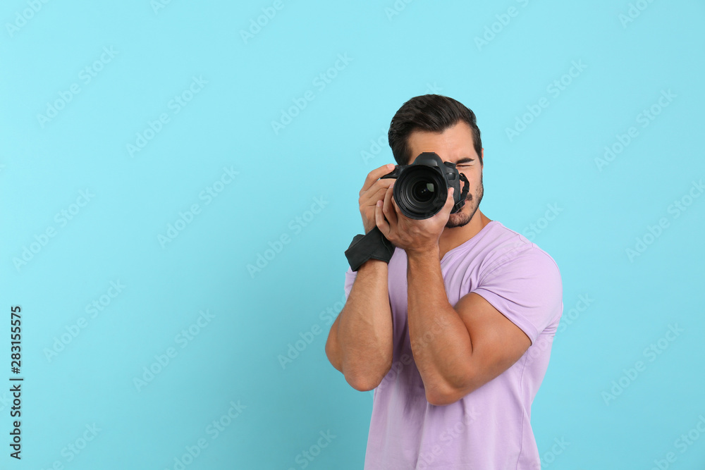 Young professional photographer taking picture on light blue background. Space for text Young professional photographer taking picture on light blue background. Space for text