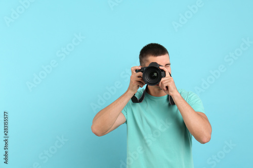 Young professional photographer taking picture on light blue background. Space for text