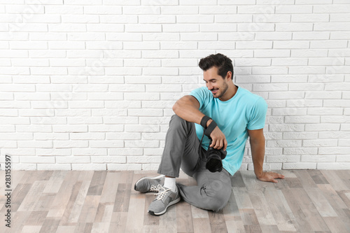 Young photographer with professional camera near brick wall. Space for text