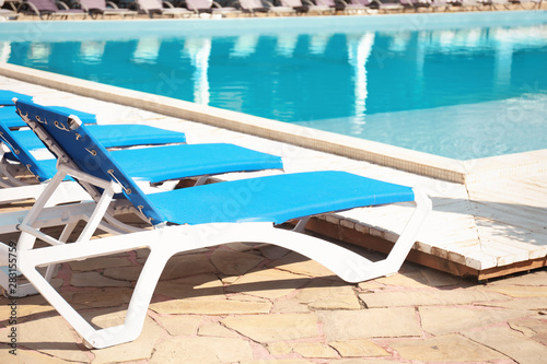 Comfortable loungers at clean swimming pool on sunny day