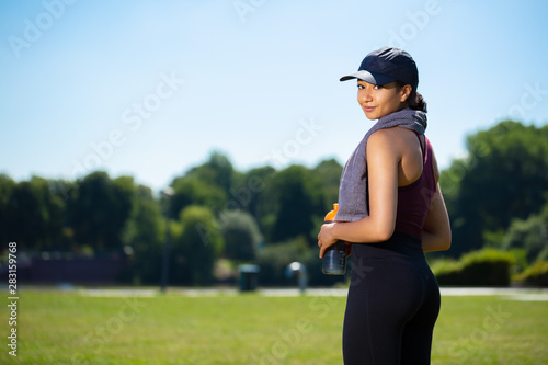 Mixed young woman with a towel and a cap after a sport session in the park in front of trees