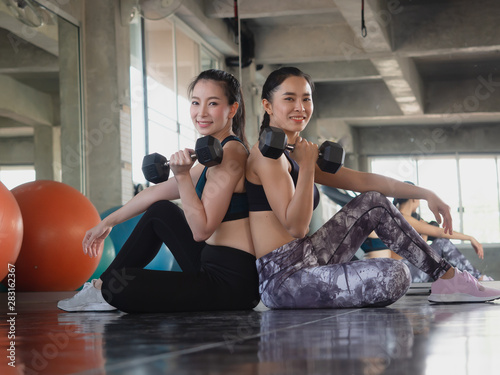 two woman is exercising with a dumbbell in gym