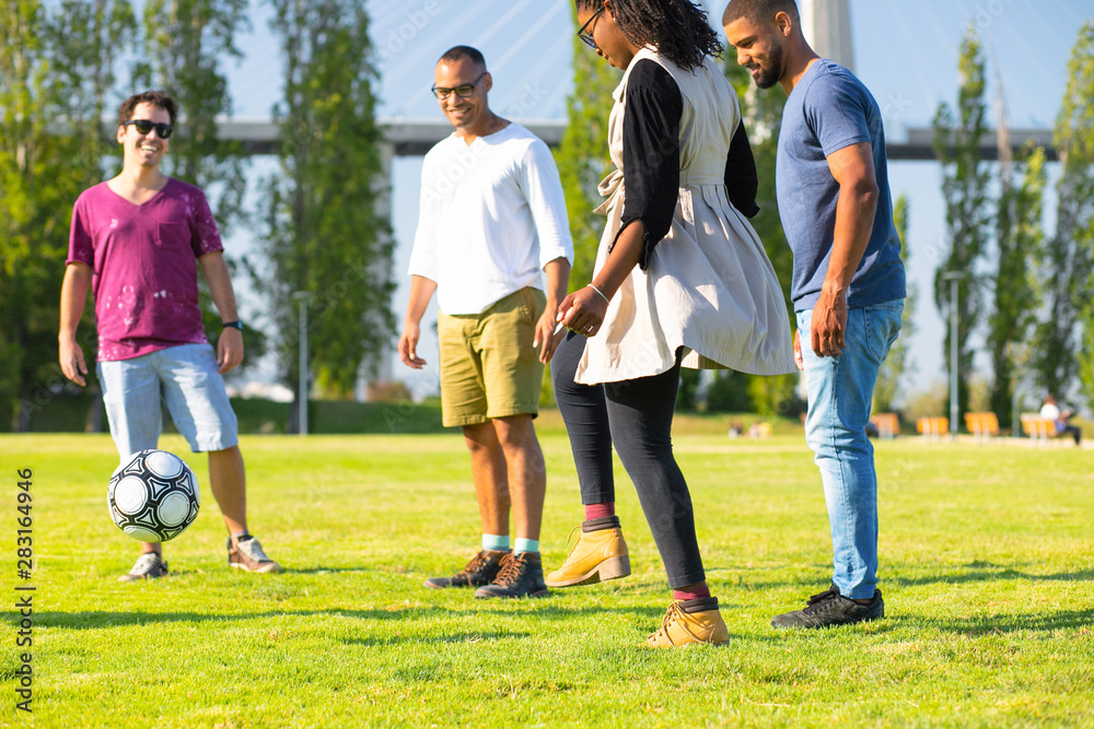 Group of four happy friends kicking ball in park. Smiling young people having fun together. Leisure concept