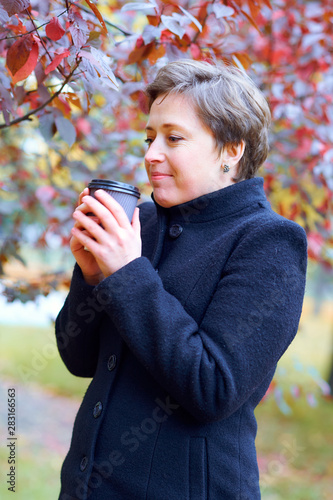 Beautiful woman posing with paper cup of tea or coffee in autumn city park  fall season