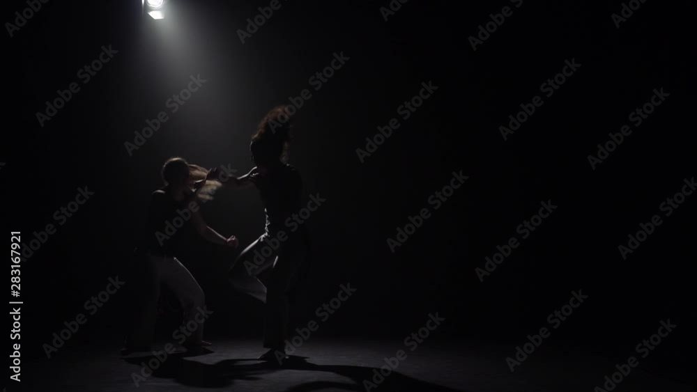 Two females practicing capoeira in darkness under spotlight in studio. Slow motion. Two females practicing capoeira in darkness under spotlight in studio. Slow motion.