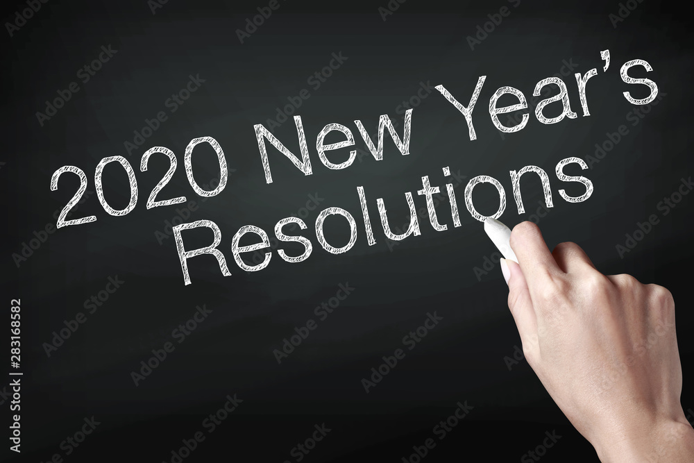 Hand holding a chalk and writing 2020 new year resolutions Hand holding a chalk and writing 2020 new year resolutions