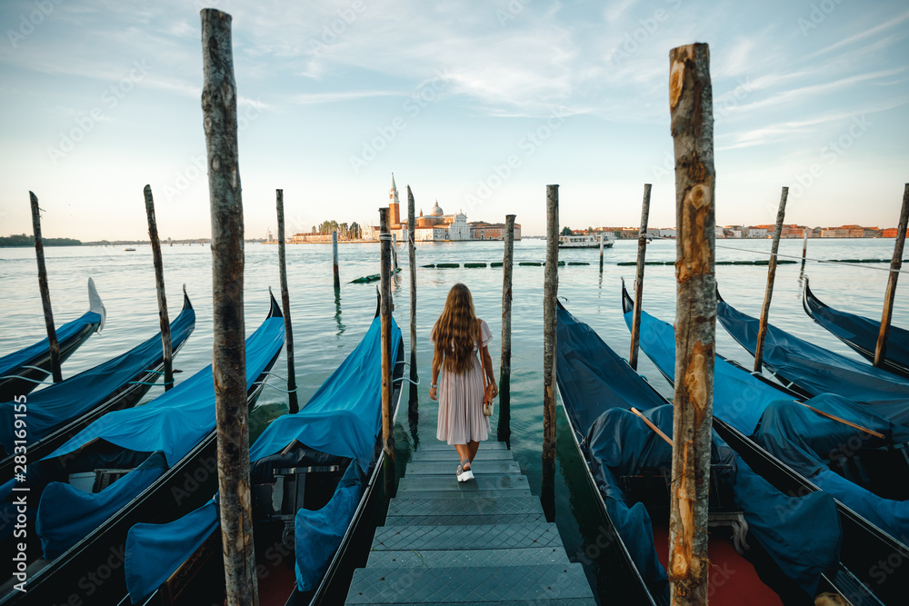 Back view youn woman tourist walking on  the pier among gondolas. Happy girl enjoying View on the Grand canal with venetian gondolas. Tour to Venice and Italy concept