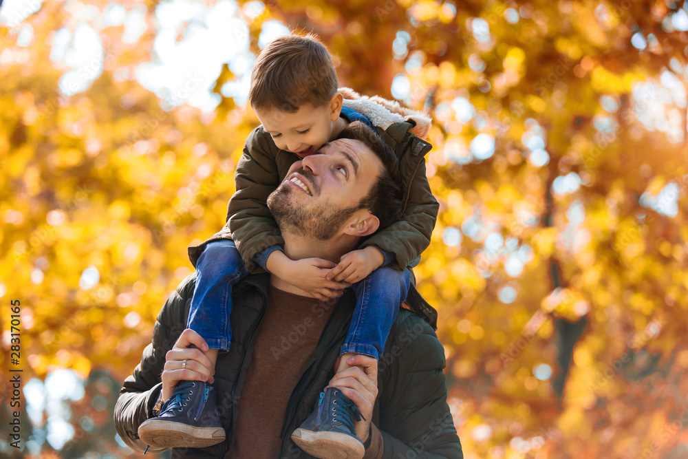 Happy father and little son playing and having fun outdoors over autumn park background - obrazy, fototapety, plakaty 