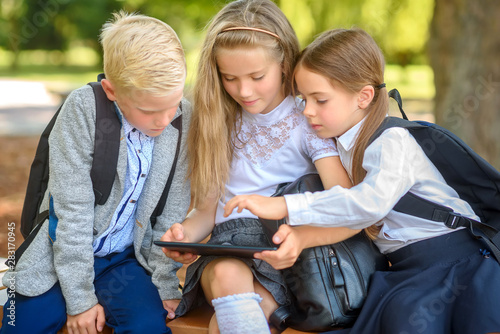 school friends, schoolchildren sitting on a bench in the park use a tablet to study lessons, social media communication