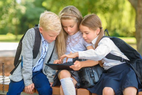 school friends, schoolchildren sitting on a bench in the park use a tablet, social media communication