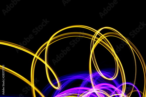Long exposure, light painting photography. Vibrant abstract streaks of neon pink and gold color against a black background.