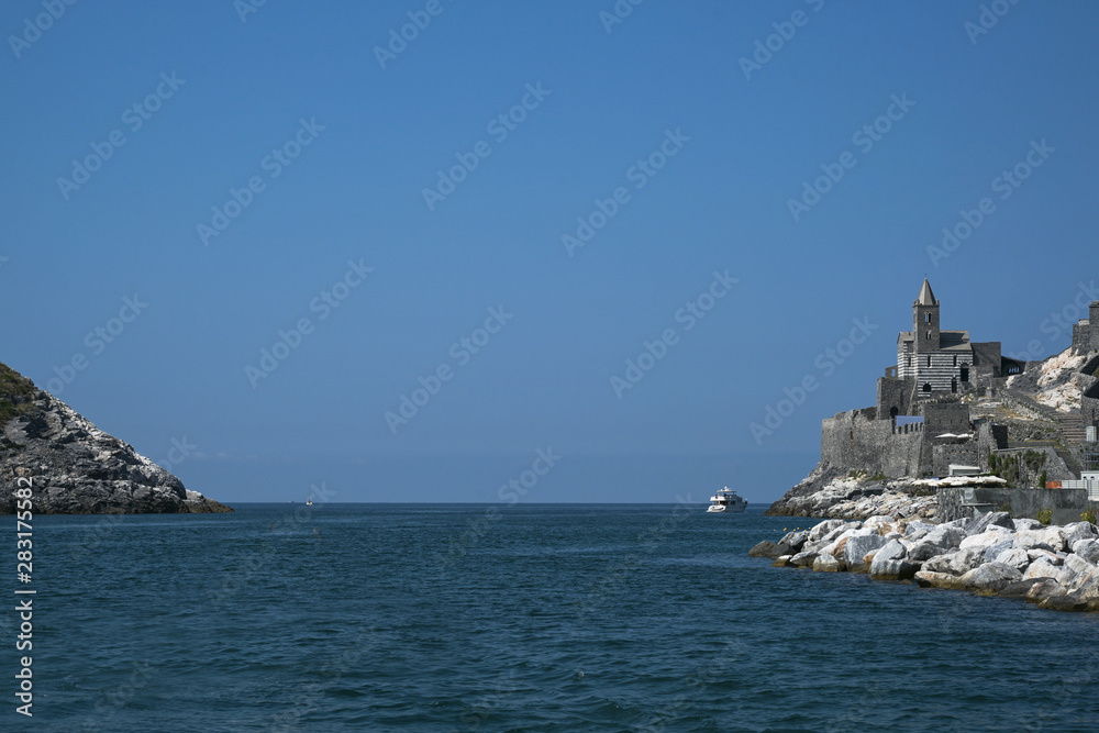 sea passage between the headland of Porto Venere with the famous Saint Peter's Church and the island of Palmaria, the gate to the Cinque Terre, Liguria, Italy, blue sky with copy space