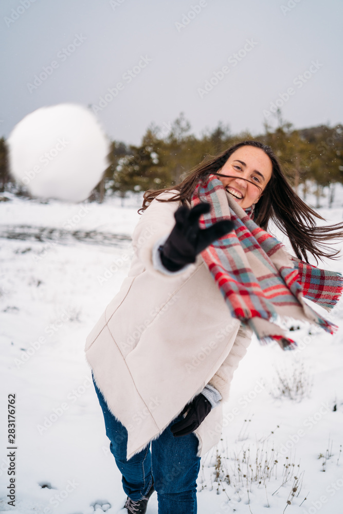 Beautiful and smiling woman dressed in a coat, throwing snowballs at the camera - Vacation concept Beautiful and smiling woman dressed in a coat, throwing snowballs at the camera - Vacation concept