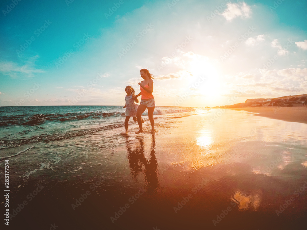 Mother and daughter running on tropical beach - Mum playing with her kid in holiday vacation next to the ocean - Family lifestyle and love concept - Focus on bodies silhouette