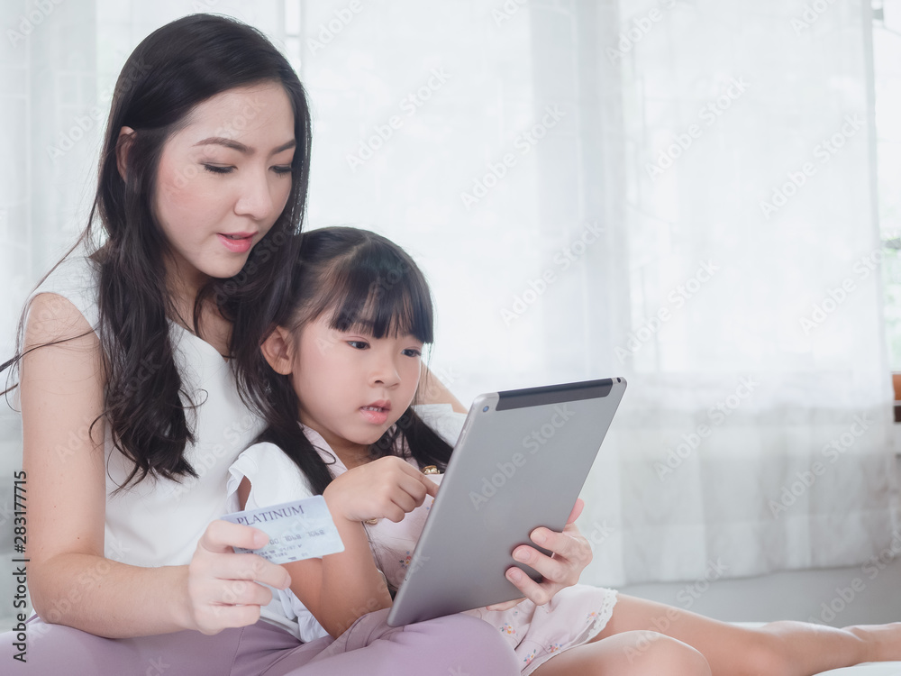 The child is playing in bed with her mother,.Mom shoppping online by credit card with her daughter on laptop The child is playing in bed with her mother,.Mom shoppping online by credit card with her daughter on laptop