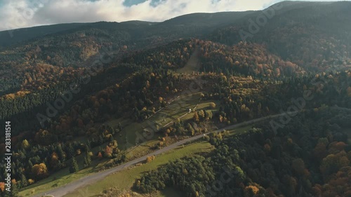 grey asphalt road surrounded by mixed forests and green meadows lit by autumn sunlight upper view. Carpathian mountains, Ukraine beauty nature. Travel, summer holidays, wild recreation. 4K photo