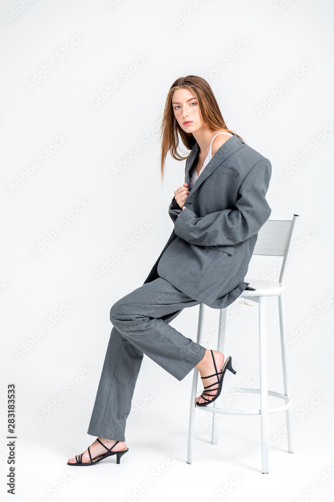 Portrait of young beautiful woman in oversized man suit on a bar chair isolated on white background Portrait of young beautiful woman in oversized man suit on a bar chair isolated on white background