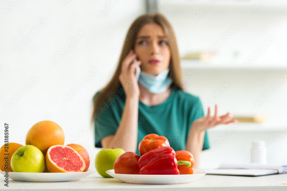 selective focus of woman in medical mask talking on smartphone at table with fruits, vegetables and pills at home selective focus of woman in medical mask talking on smartphone at table with fruits, vegetables and pills at home