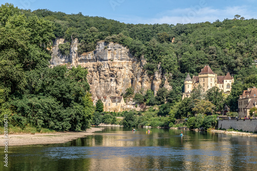 La Roque Gageac, one of France's most beautiful villages by the Dordogne River, backed by a steep hill / cliff, Malartrie Castle in the background. Canoeing on the river. Travel France.