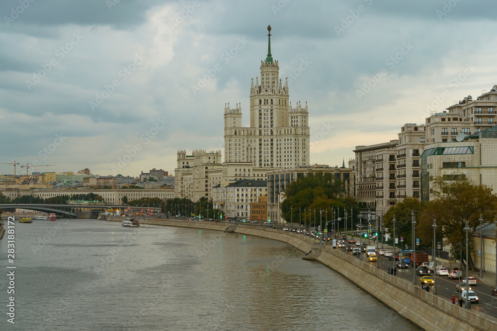 Moscow cityscape at summer day. Stalinist neoclassical style house on the Kotelnicheskaya embankment, Bolshoy Ustinsky Bridge. Active movement of ships, Moskva River